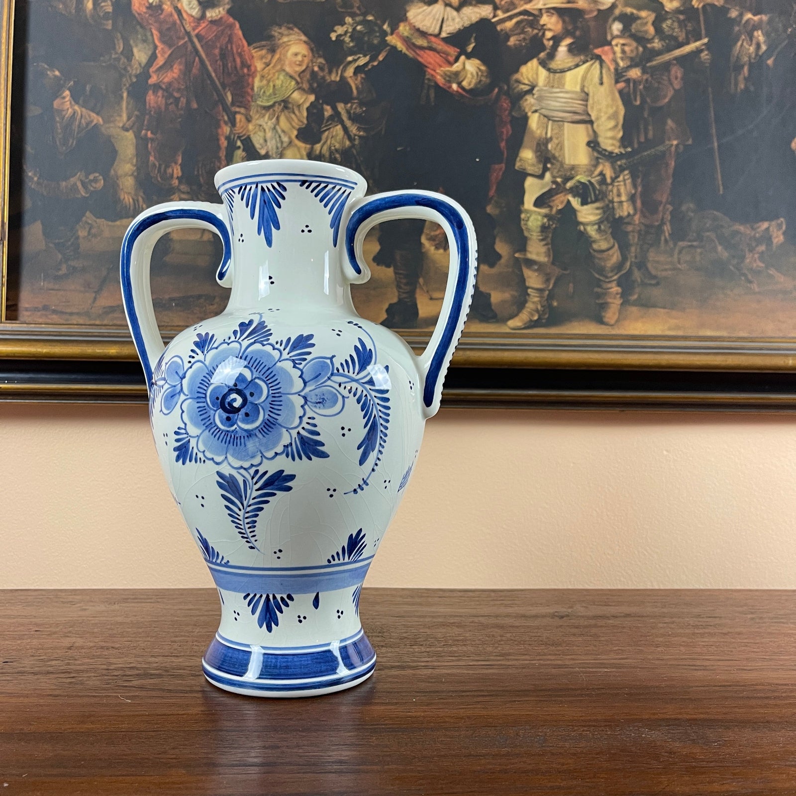 Blue and white floral-patterned vase on a wooden surface with a painting in the background