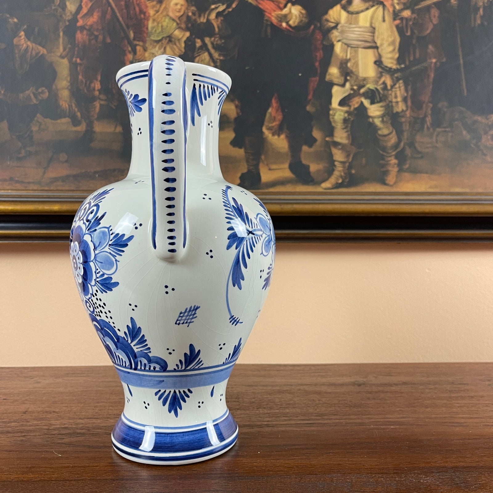 Blue and white ceramic vase on a wooden surface with a painting in the background