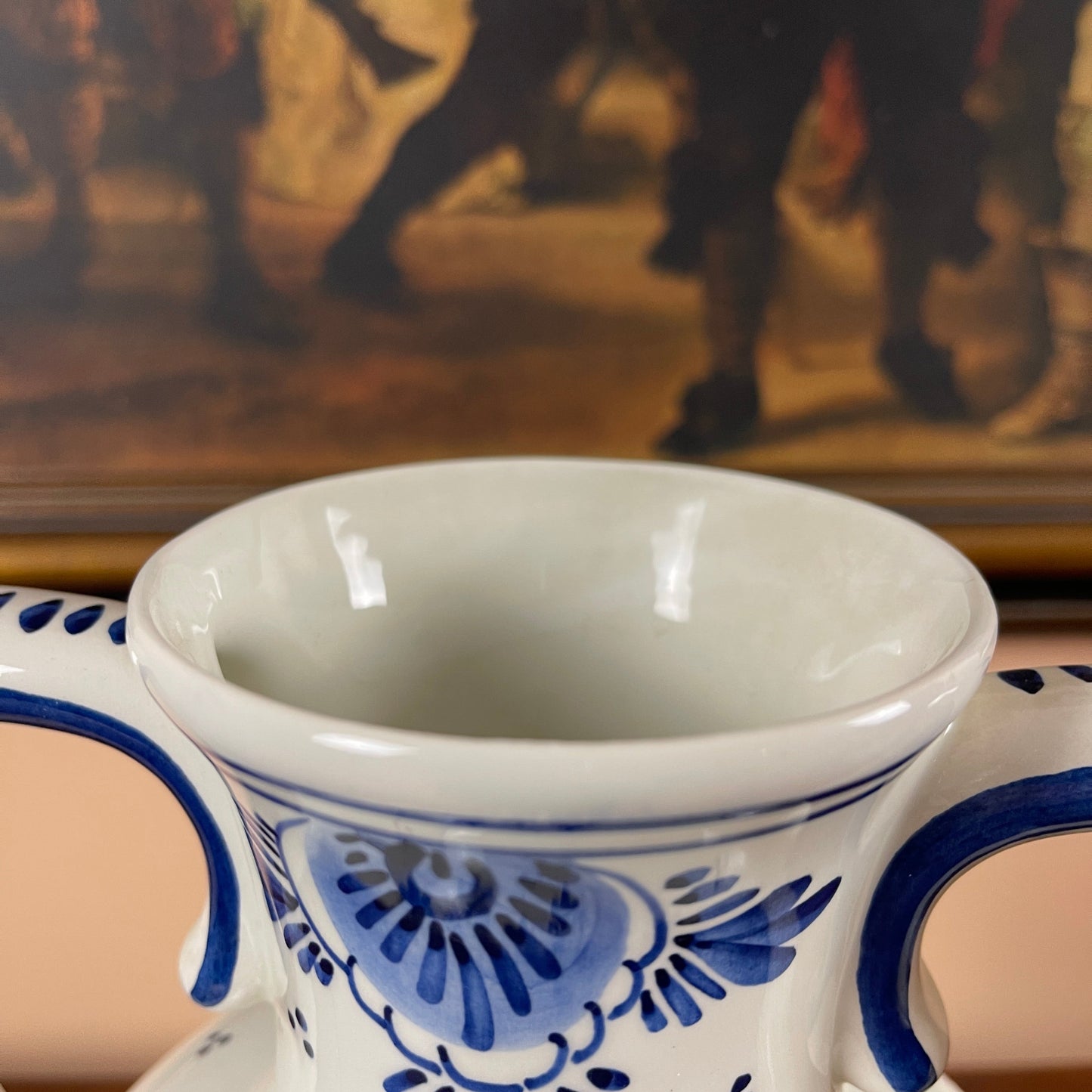 White mug with blue decorative patterns in front of a blurred painting