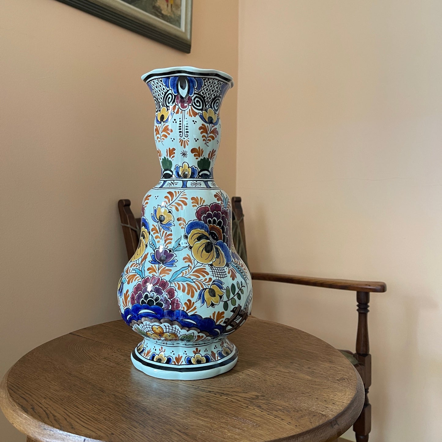 Decorative vase with floral patterns on a wooden table against a beige wall.