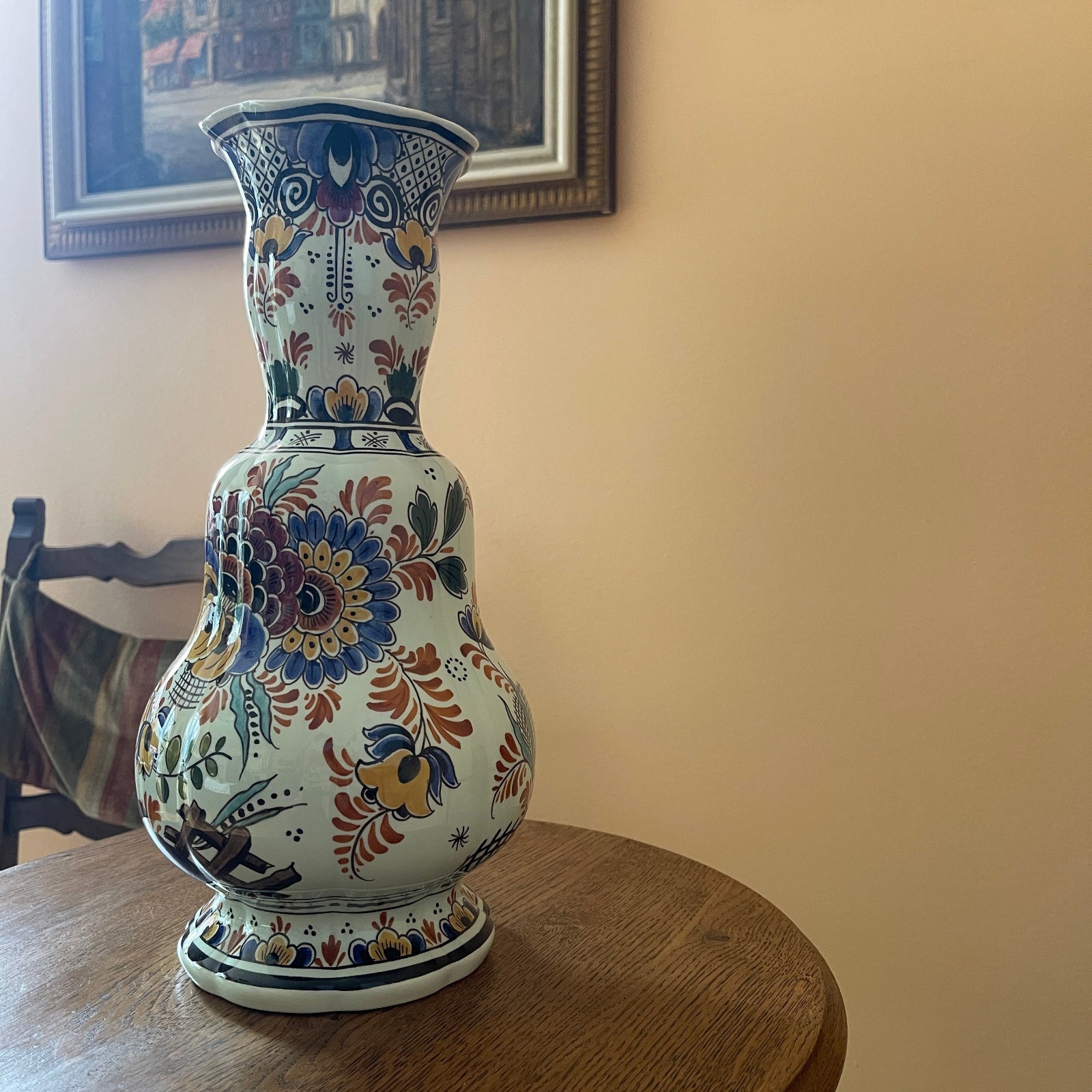 Decorative vase with floral patterns on a wooden table against a beige wall.