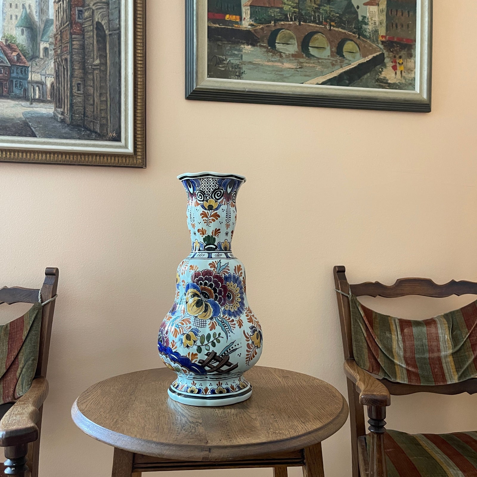 Decorative vase on a table with chairs and framed pictures in the background