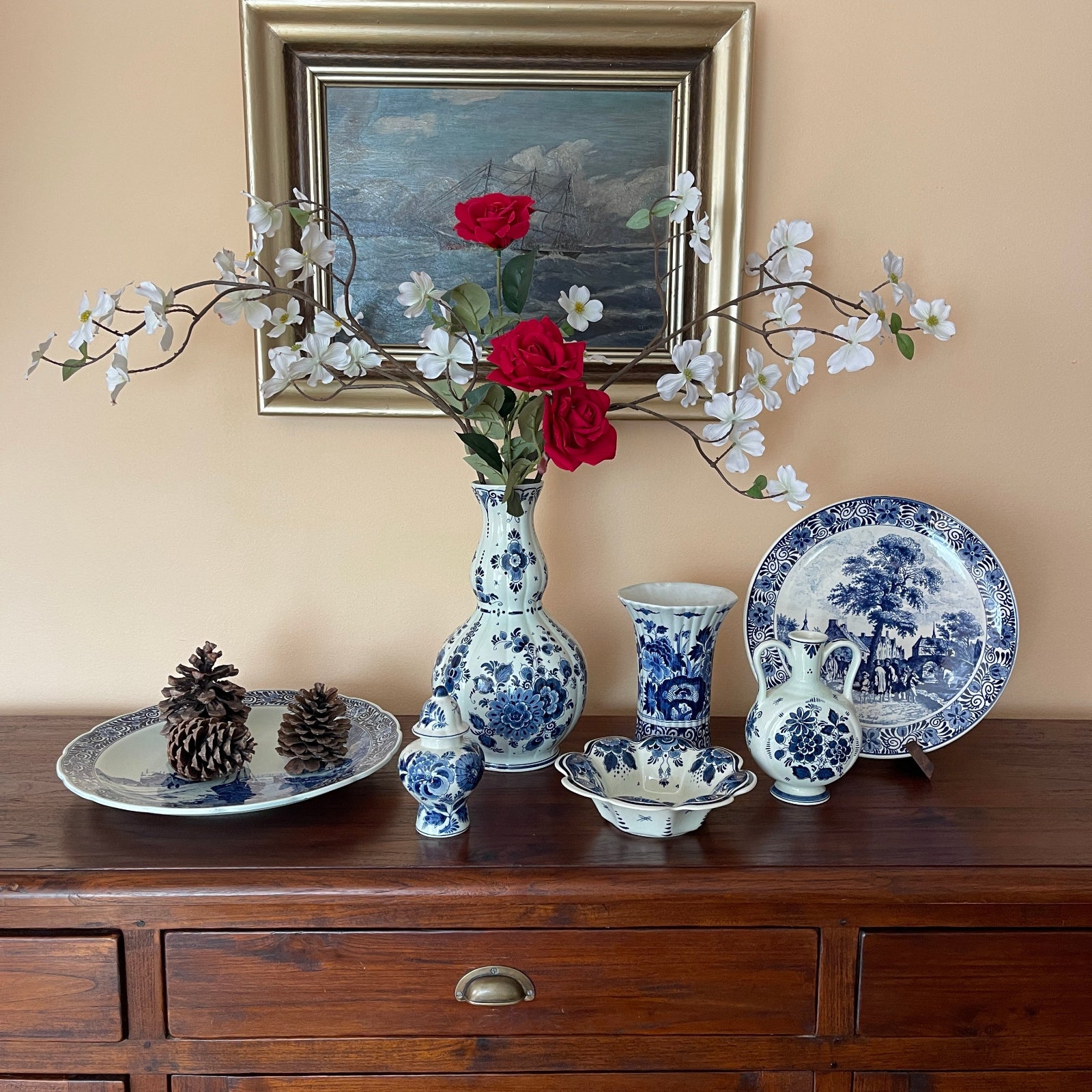 Decorative items including vases, plates, and flowers on a wooden surface with a painting in the background.