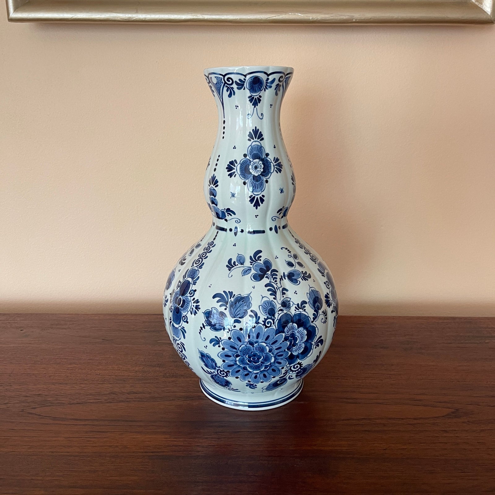 Blue and white floral patterned vase on a wooden surface with a beige wall background