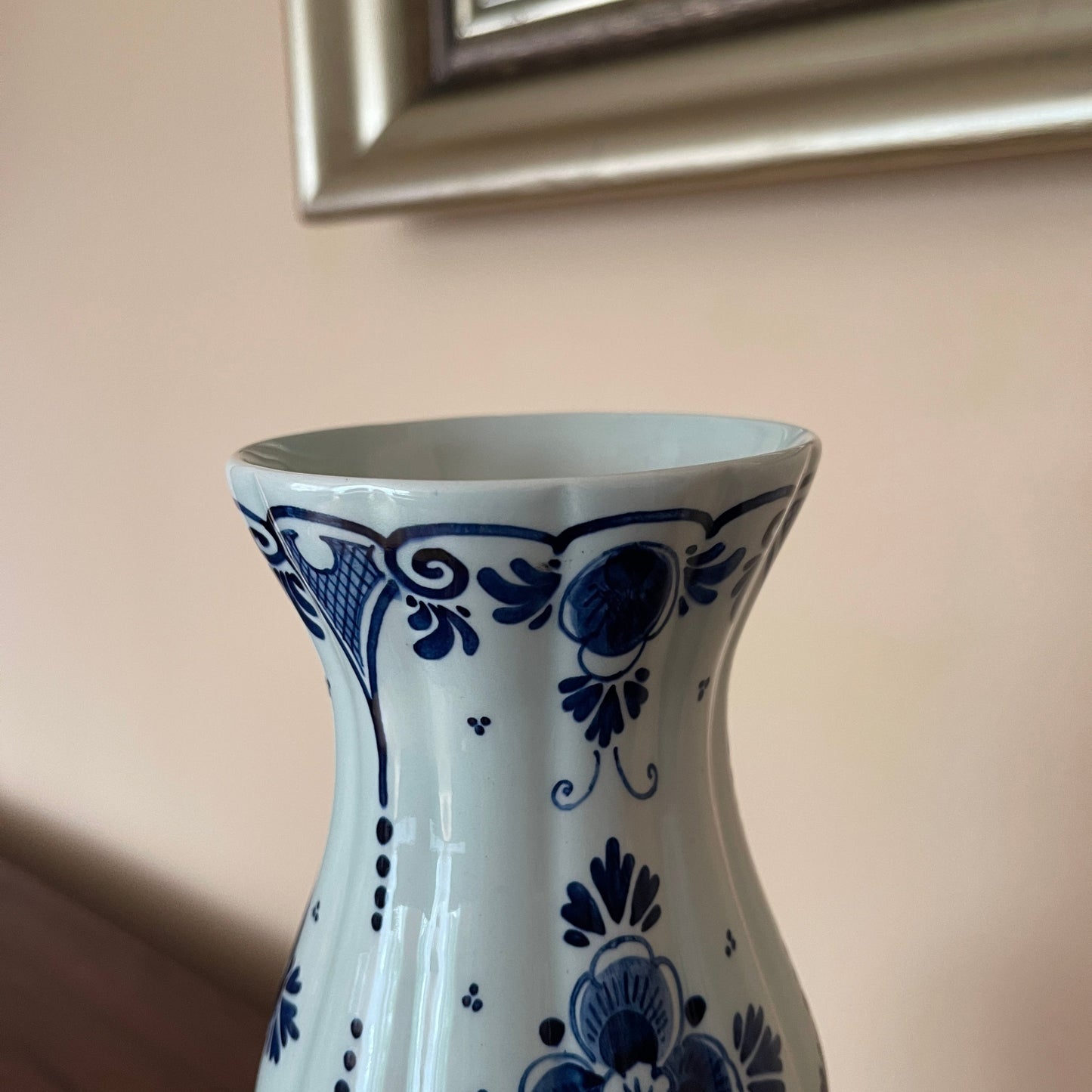 White vase with blue floral patterns against a beige wall.