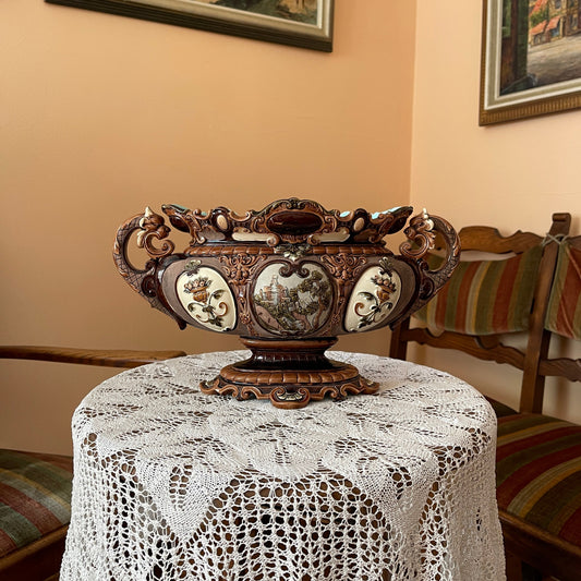 Decorative wooden vase on a table with a lace tablecloth, framed pictures on the wall.