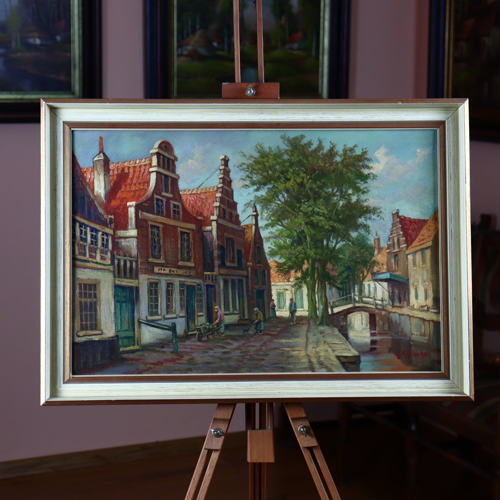 An oil painting depicting a canal-side scene with houses and trees, signed by G. A. Brummer, displayed in a frame.