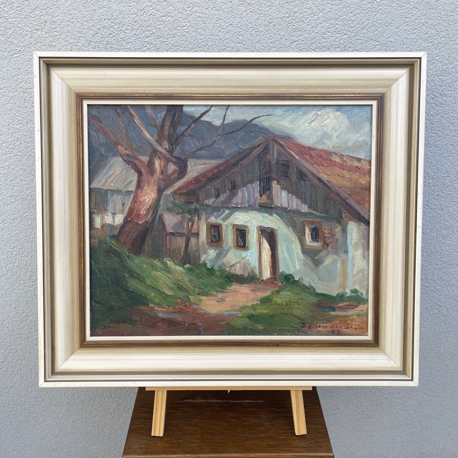 Framed painting of a rustic house with a tree on a gray wall