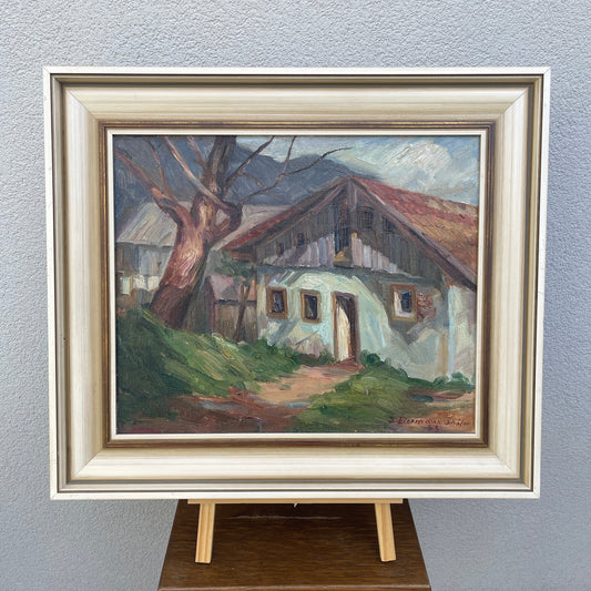 Framed painting of a rustic house with a tree on a gray wall
