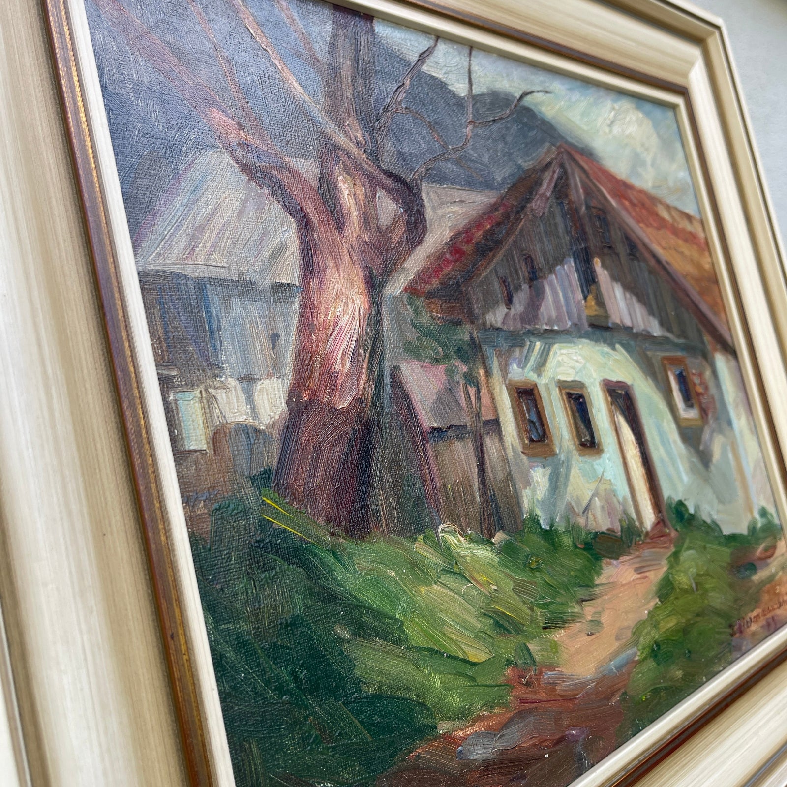 Painting of a rustic house with a tree in front, framed in gold.