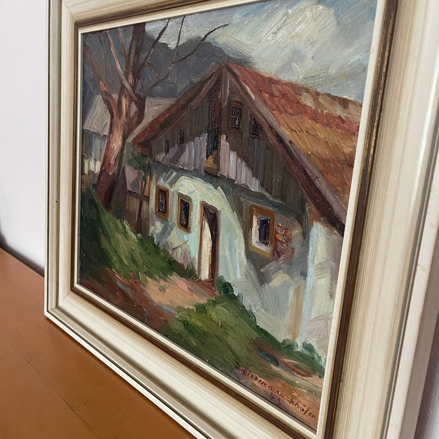 Framed oil painting of a house with a tree on a wall.