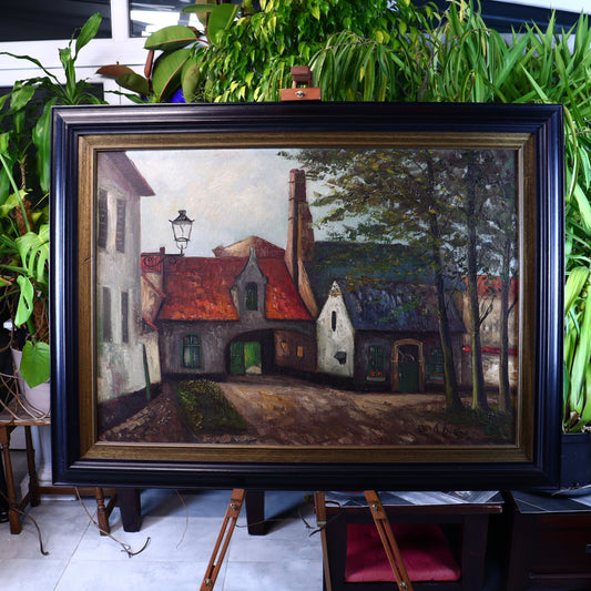 A framed oil painting of suburban buildings, featuring a street scene with houses, trees, and a lamp post, displayed in a room with plants and furniture.