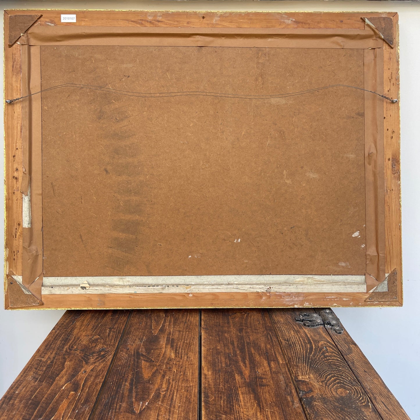 Back view of a wooden picture frame on a wooden surface with a white wall background.