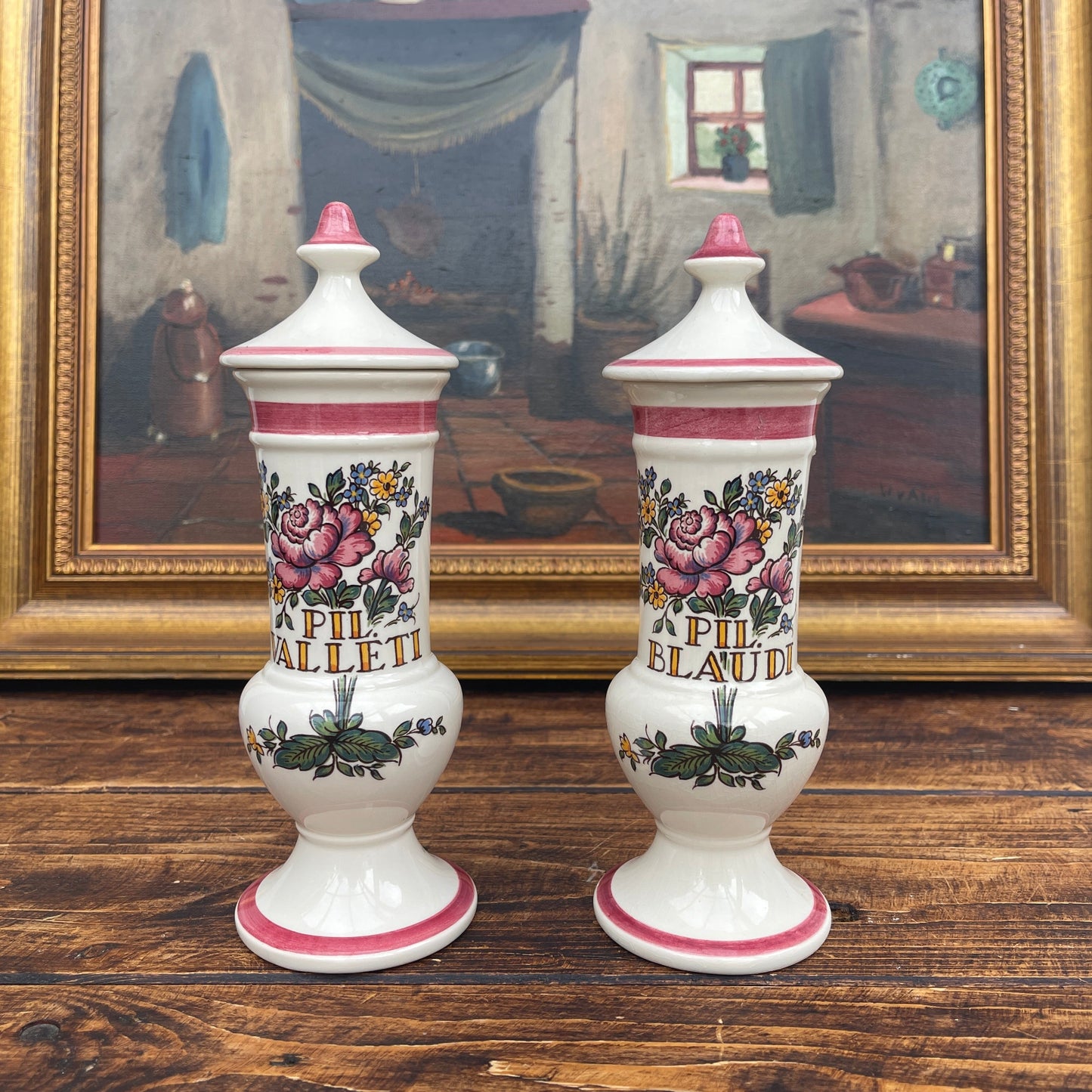 Two decorative ceramic jars with floral designs on a wooden surface, framed painting in the background.