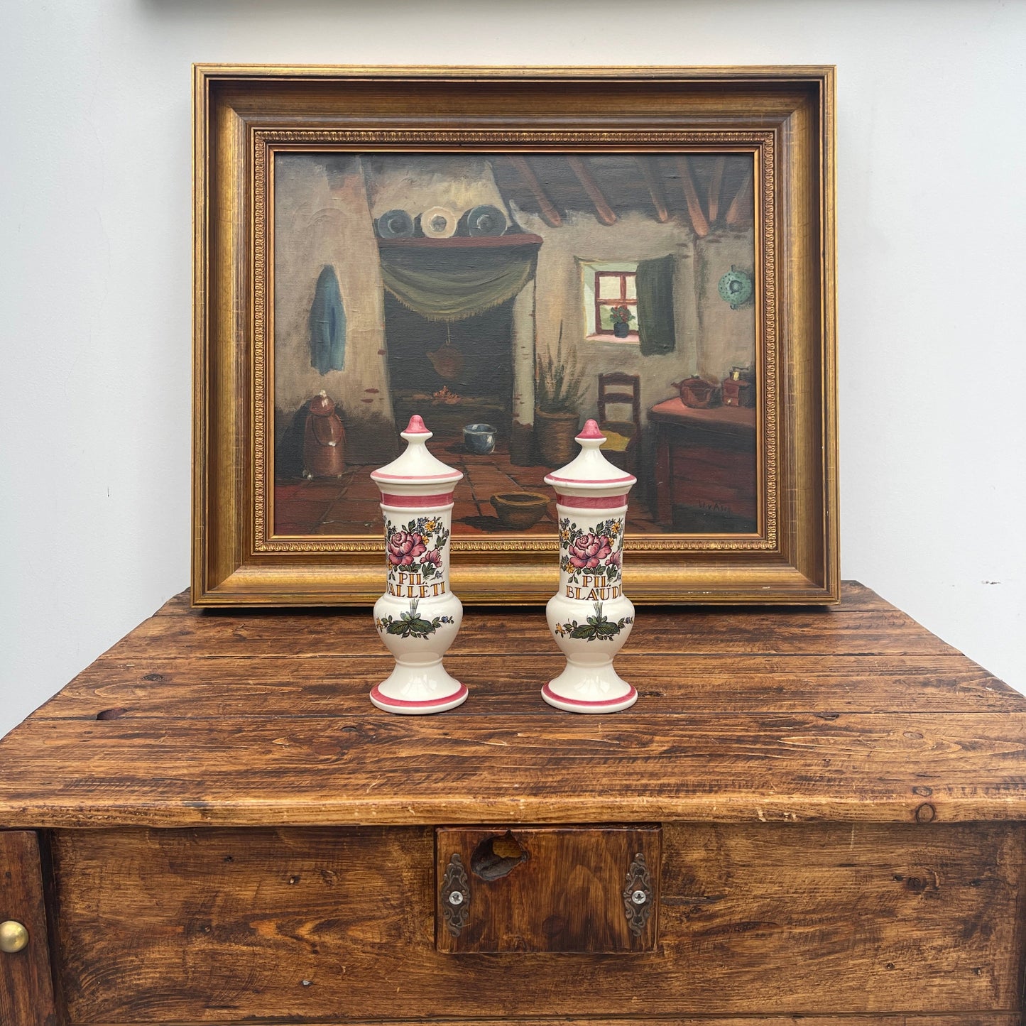 Two decorative vases on a wooden surface with a framed painting in the background.