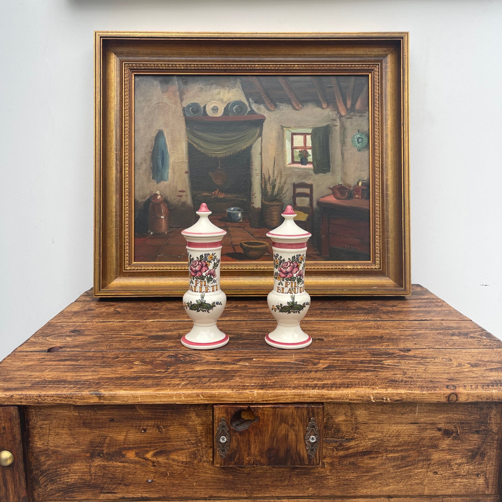 Two decorative vases on a wooden surface with a framed painting in the background.