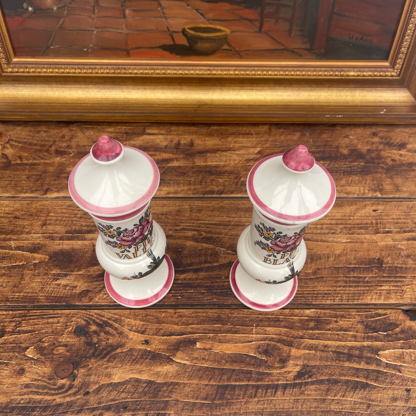 Two decorative vases with floral patterns on a wooden surface, framed artwork in the background.