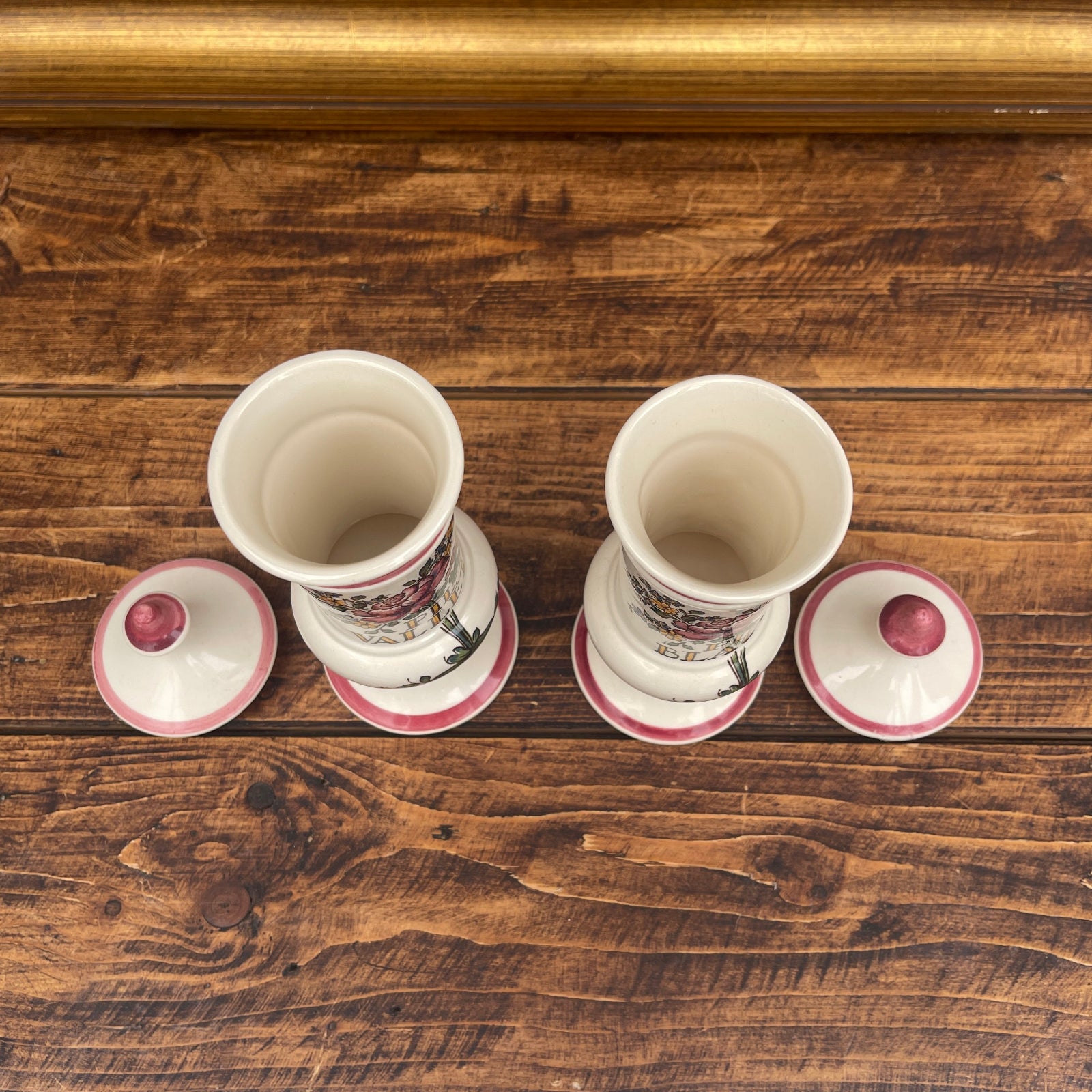 Two white ceramic cups with pink lids on a wooden surface