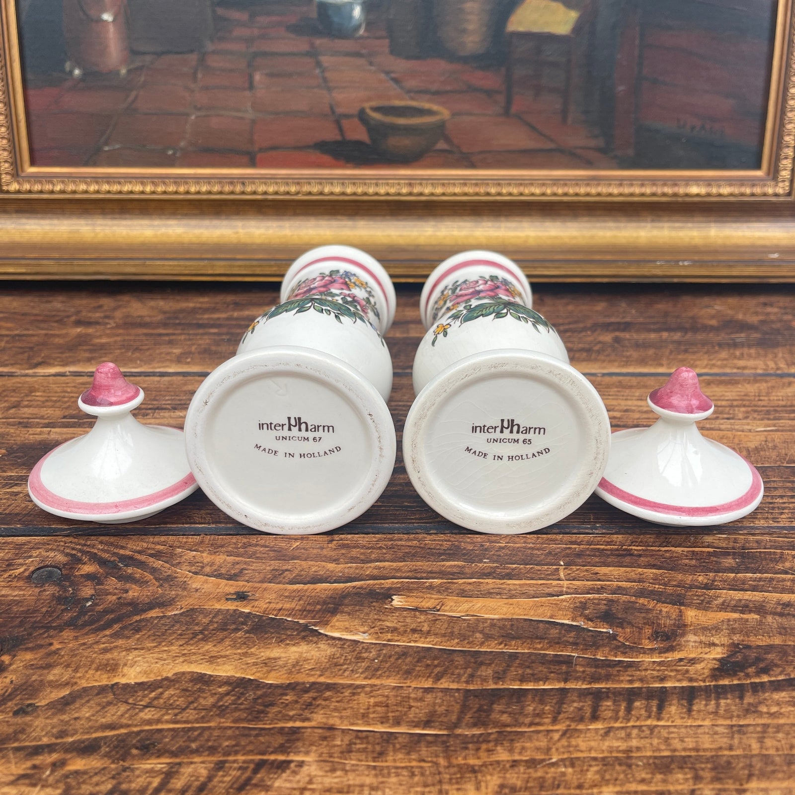 Set of decorative jars with floral designs on a wooden surface, framed artwork in the background.