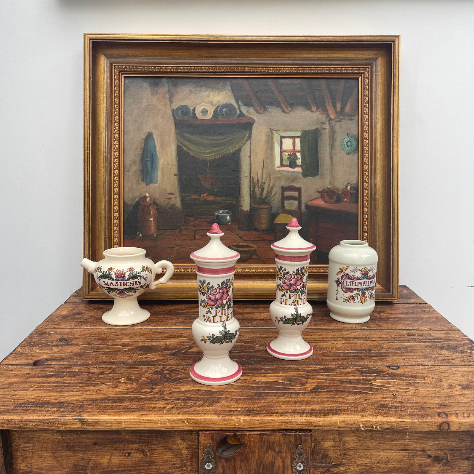 Four decorative ceramic jars on a wooden table with a framed painting in the background.