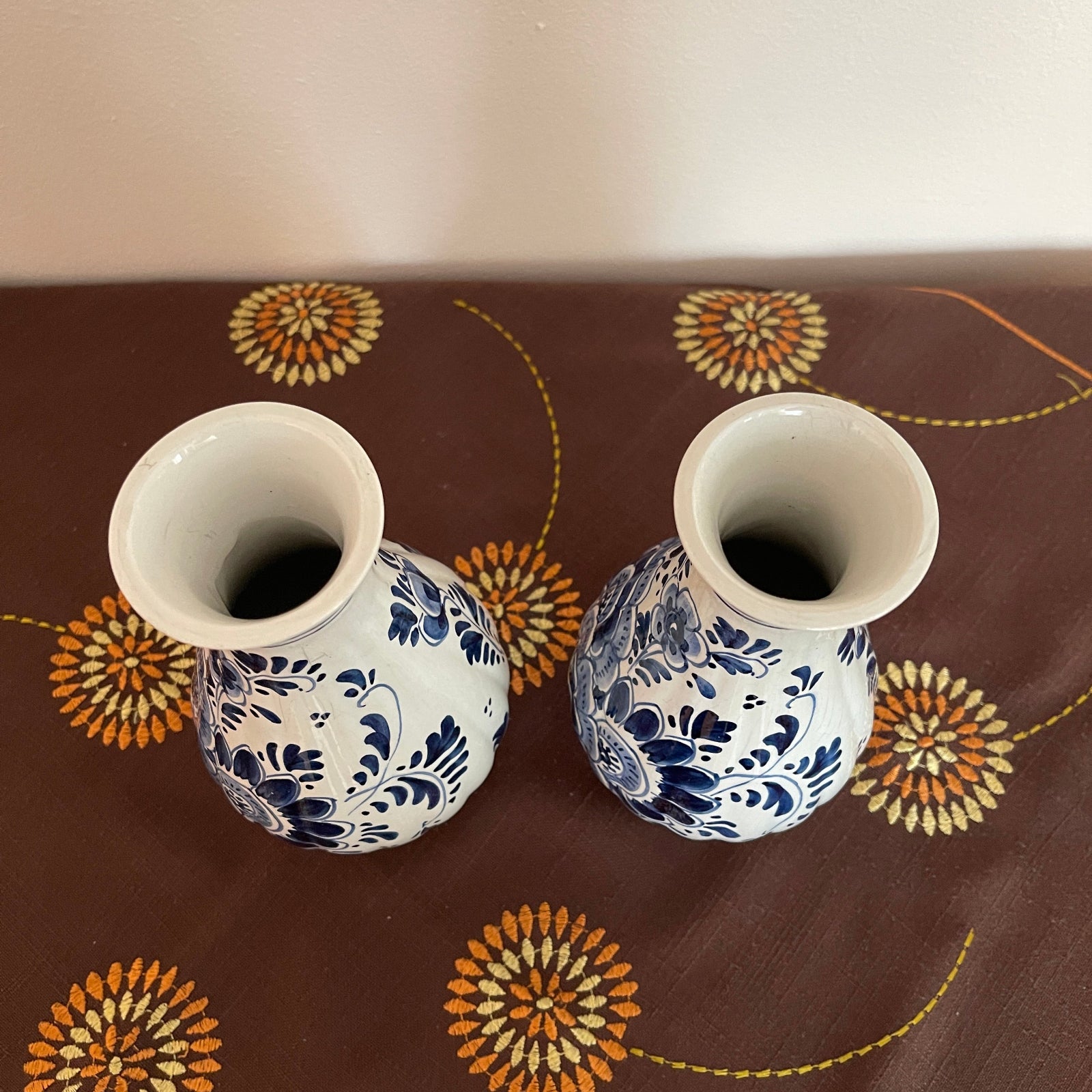 Two ceramic vases with blue floral patterns on a brown tablecloth with decorative designs.