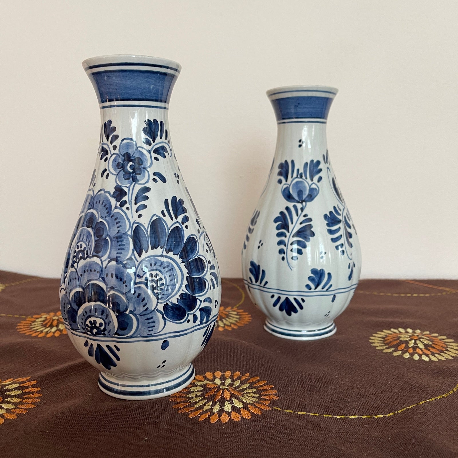 Two ceramic vases with blue floral patterns on a patterned tablecloth.