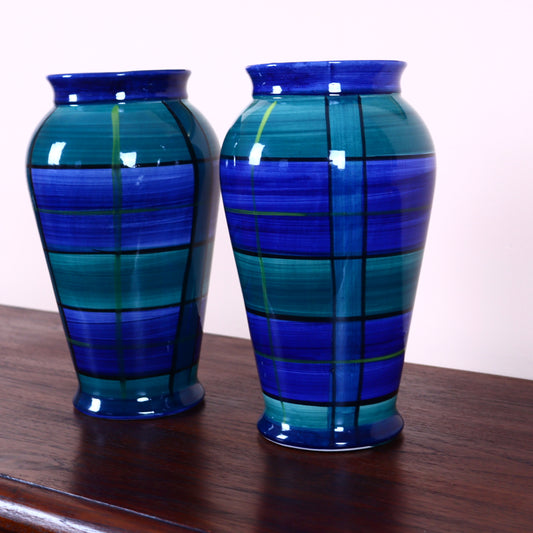 Two ceramic vases with green and navy blue geometric patterns on a table.