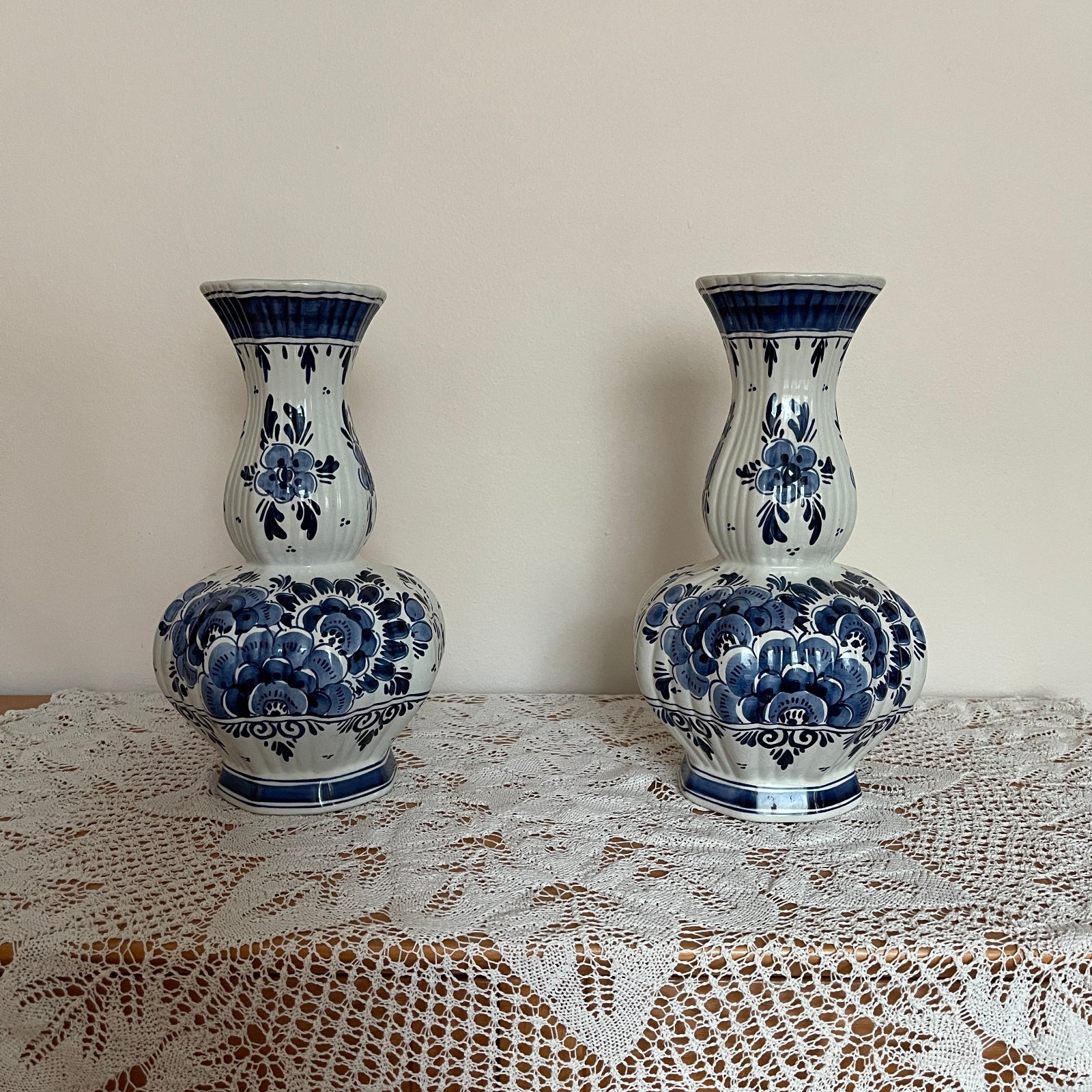 Two blue and white ceramic vases on a lace tablecloth with a plain wall background