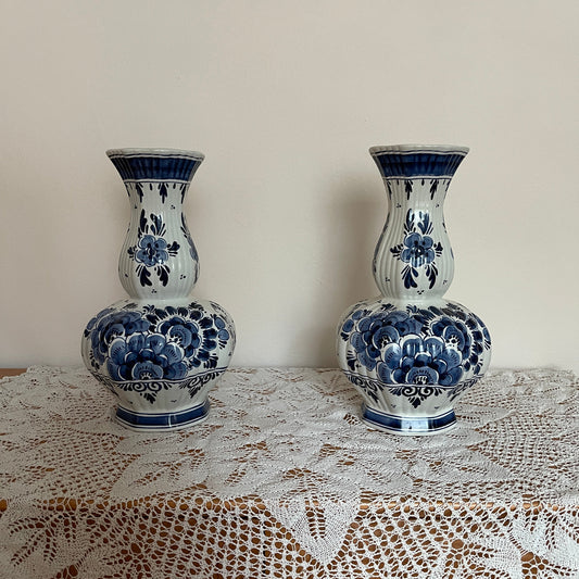 Two blue and white ceramic vases on a lace tablecloth with a plain wall background