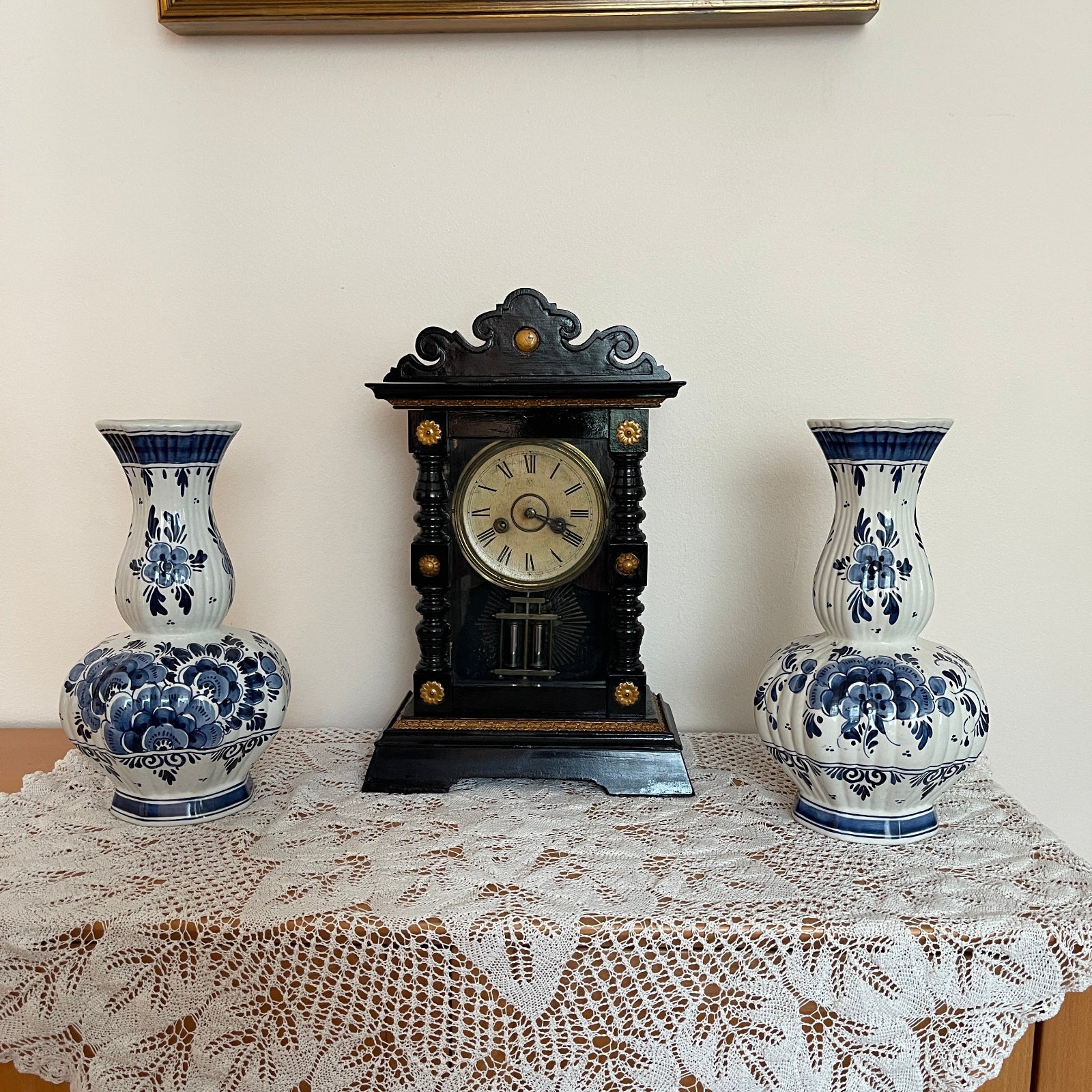 Decorative clock with two matching blue and white vases on a lace tablecloth.