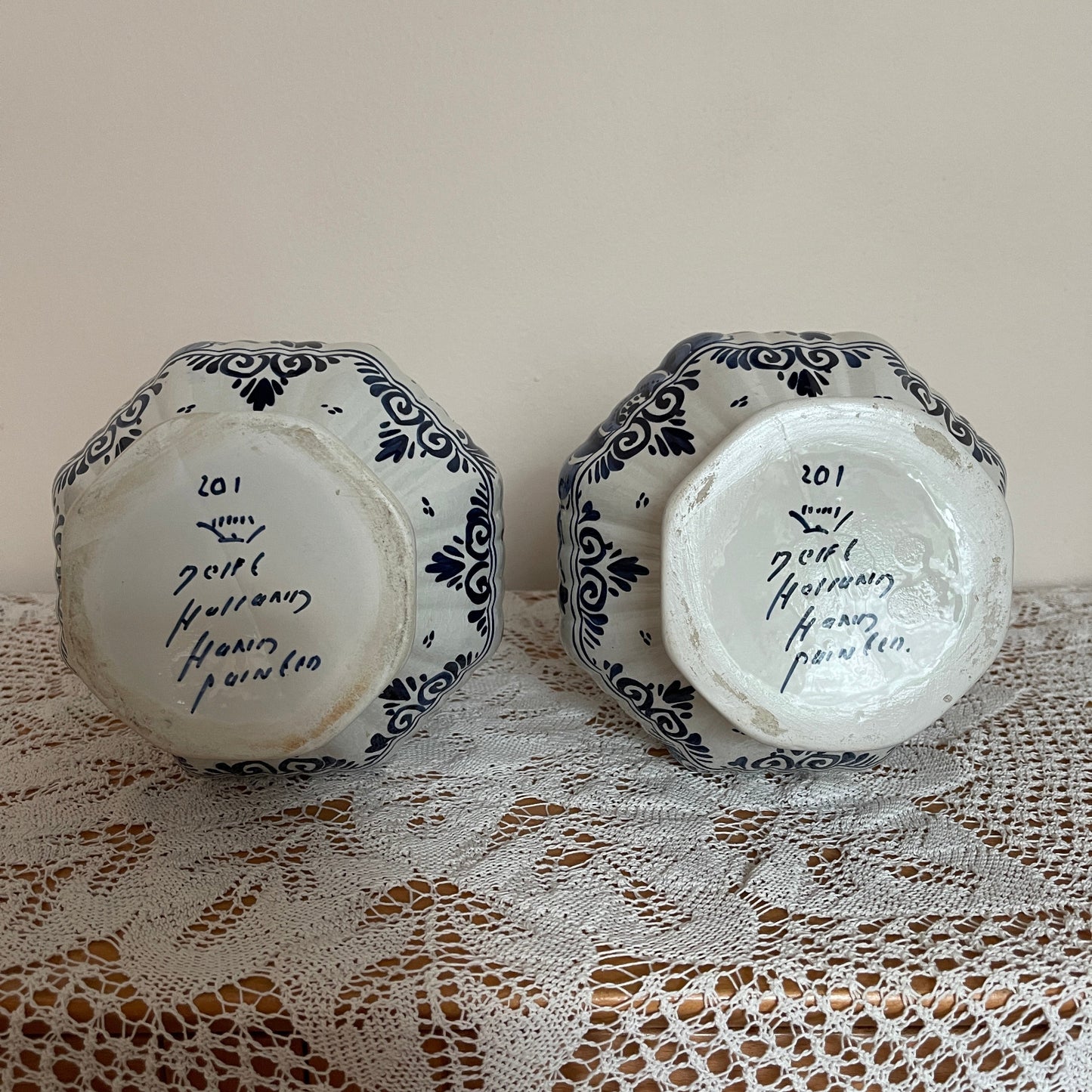 Two ceramic hexagonal plates with black patterns and text on a lace tablecloth.