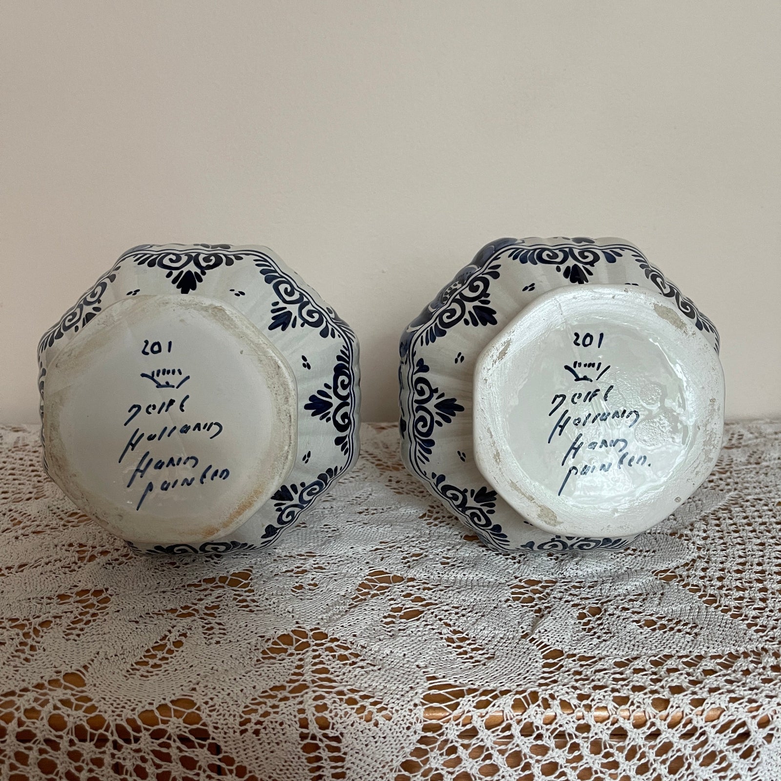 Two ceramic hexagonal plates with black patterns and text on a lace tablecloth.