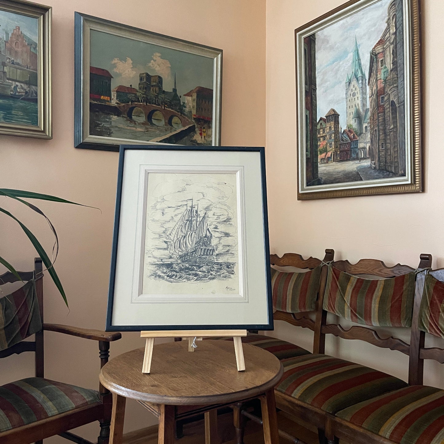 Framed artwork on a small round table with chairs and more framed pictures in the background.
