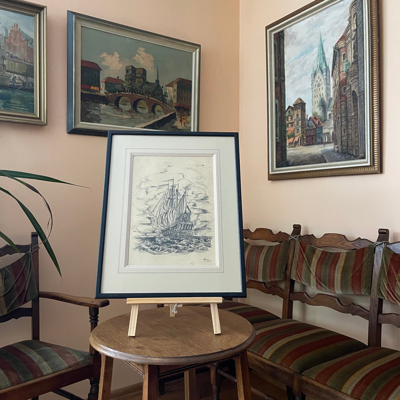 Framed artwork on a small round table with chairs and more framed pictures in the background.