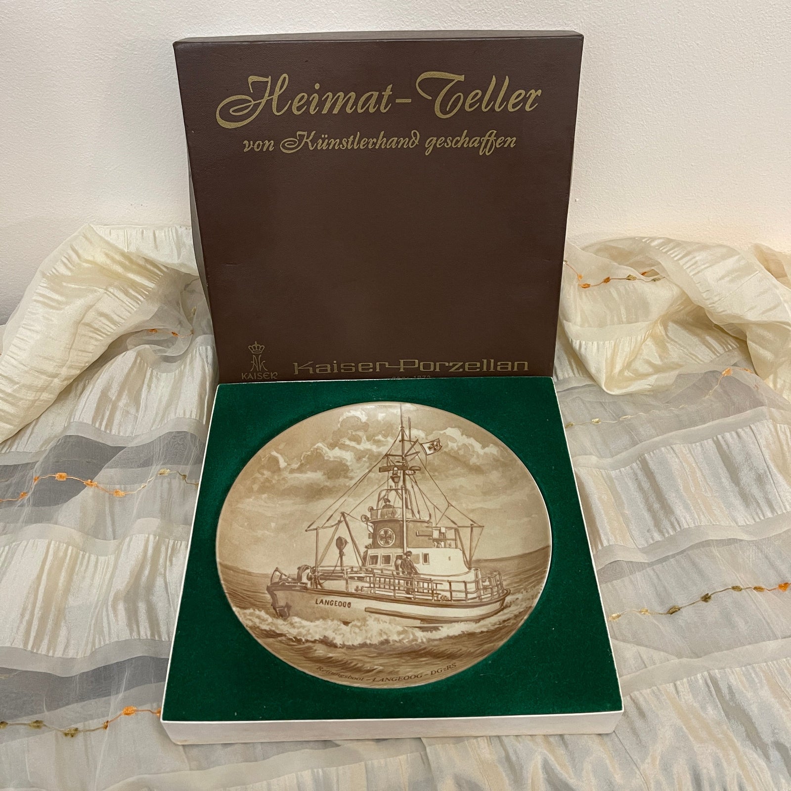 Decorative plate with ship design in a green box on a patterned fabric background