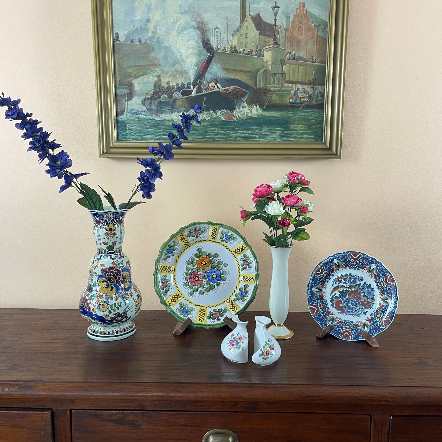Decorative ceramic items including vases and plates on a wooden surface with a painting in the background.