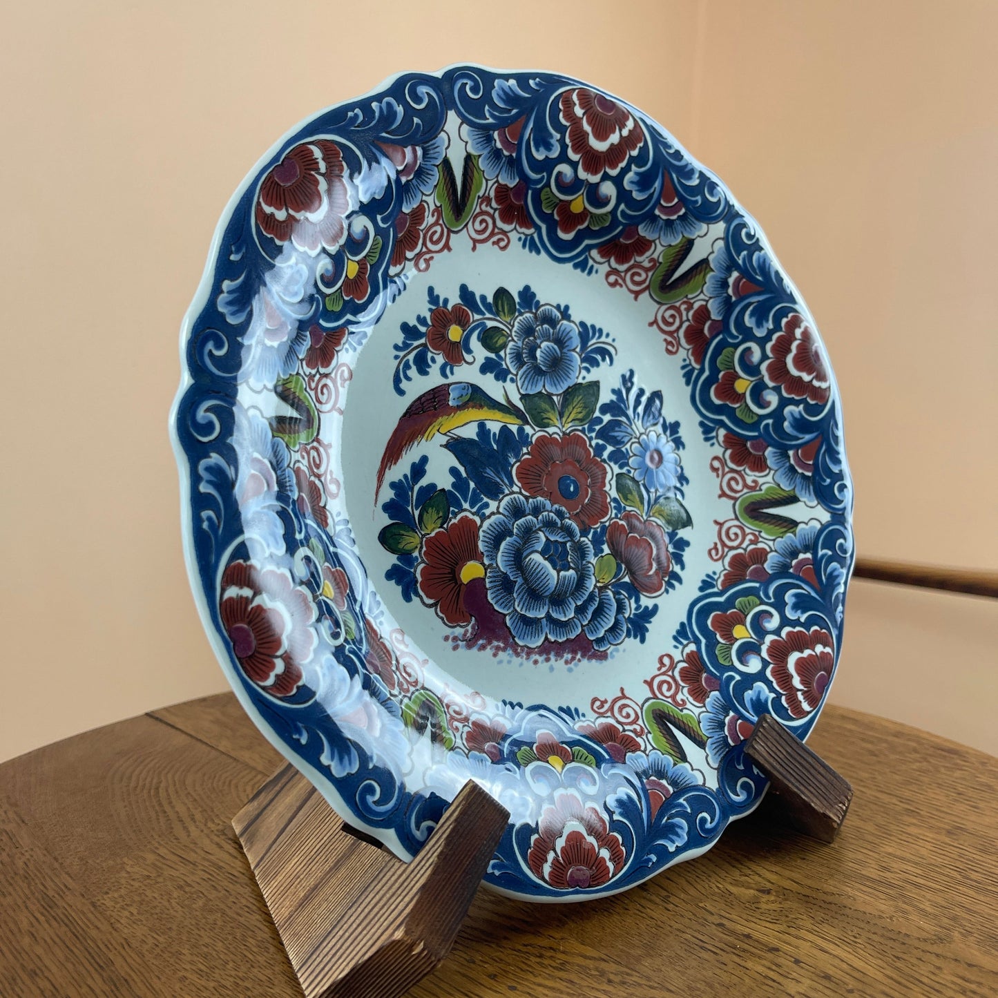 Decorative ceramic plate with floral patterns on a wooden stand against a beige background