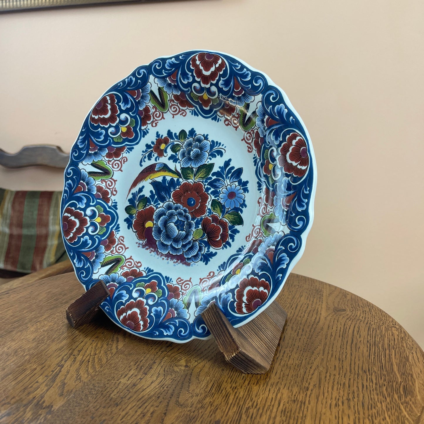 Decorative plate with floral patterns on a wooden stand against a beige wall.
