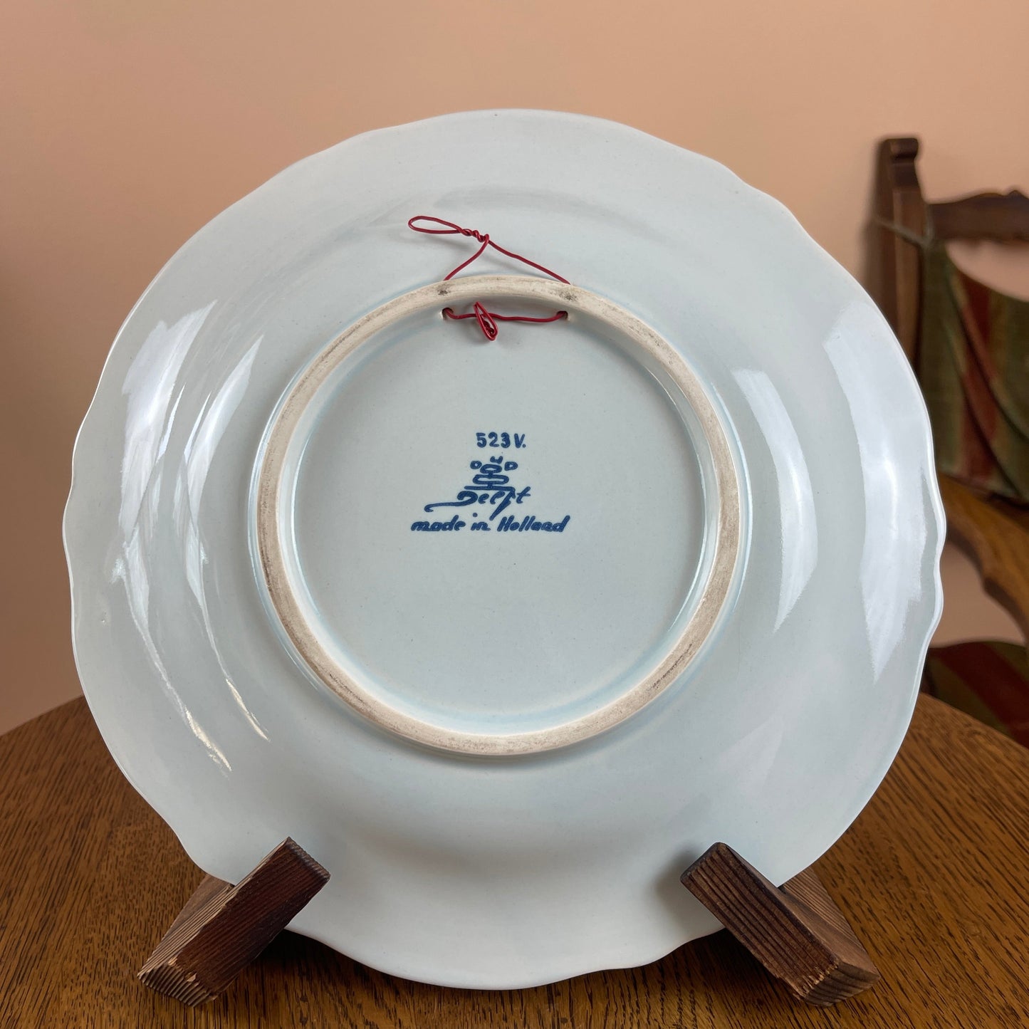 White ceramic plate with blue text on a wooden stand against a beige wall.