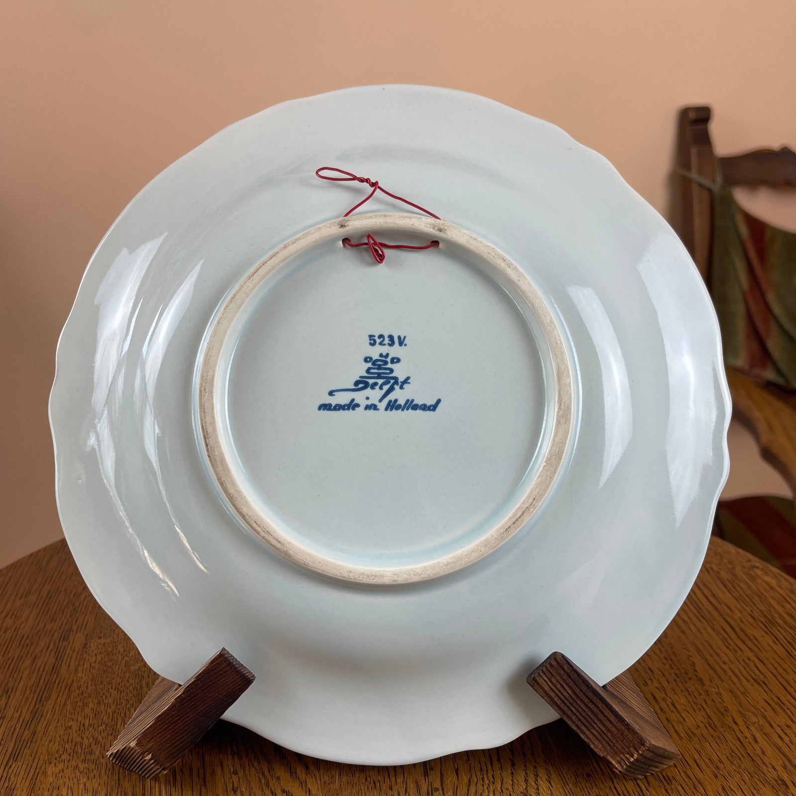 White ceramic plate with blue text on a wooden stand against a beige wall.