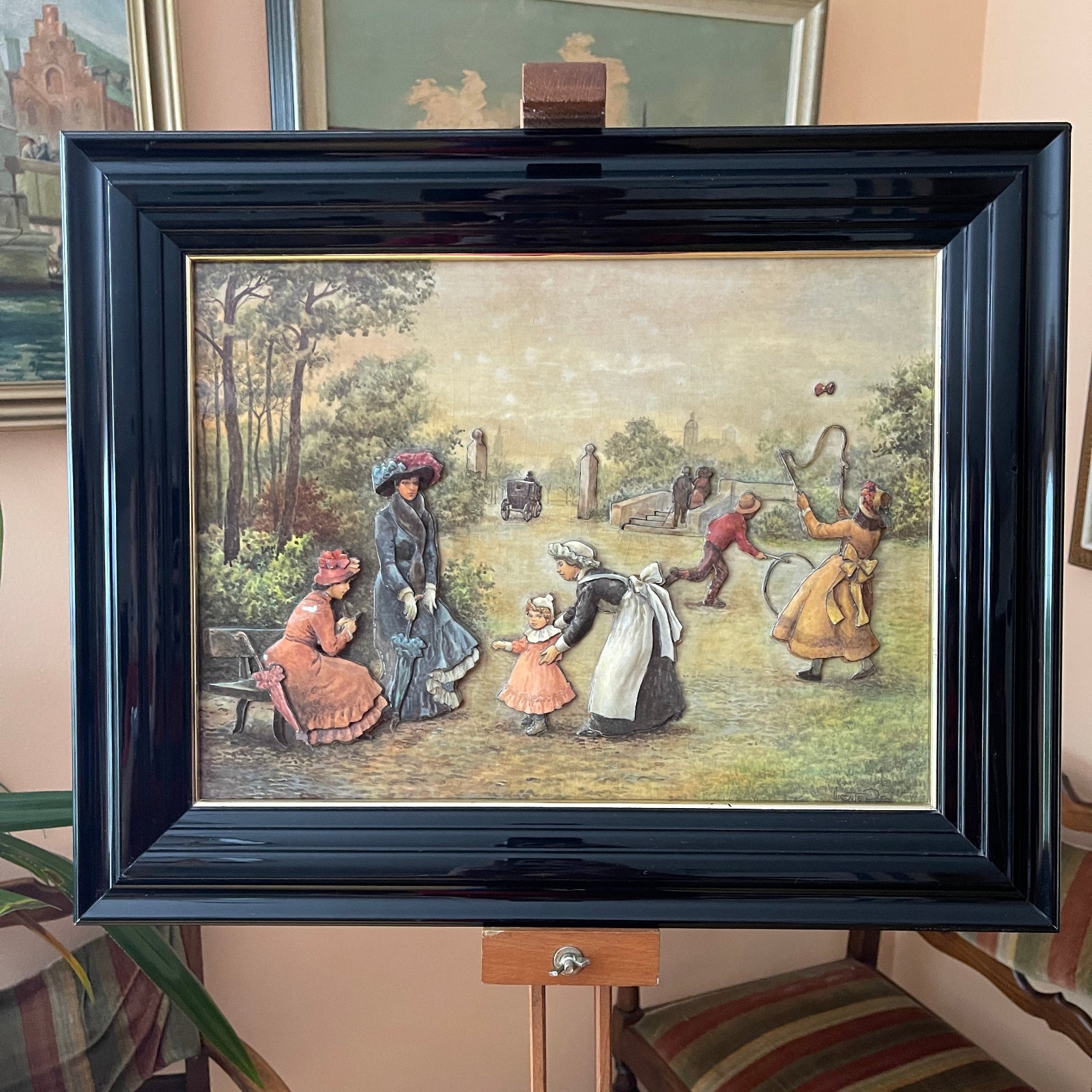 Framed artwork depicting a scene with people in a park, on a stand.