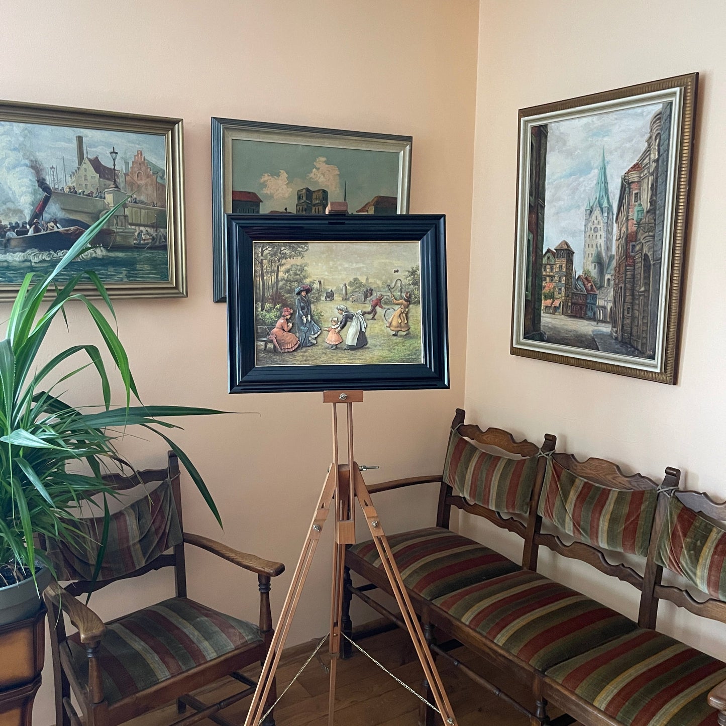 Room with framed paintings on the wall, a wooden easel, and striped chairs.