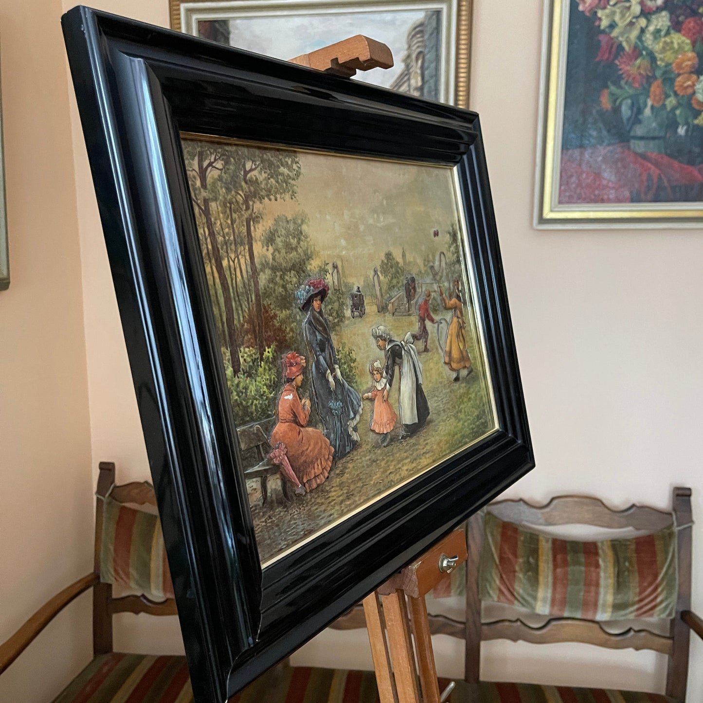 Framed painting of a scene with people in a park on an easel.