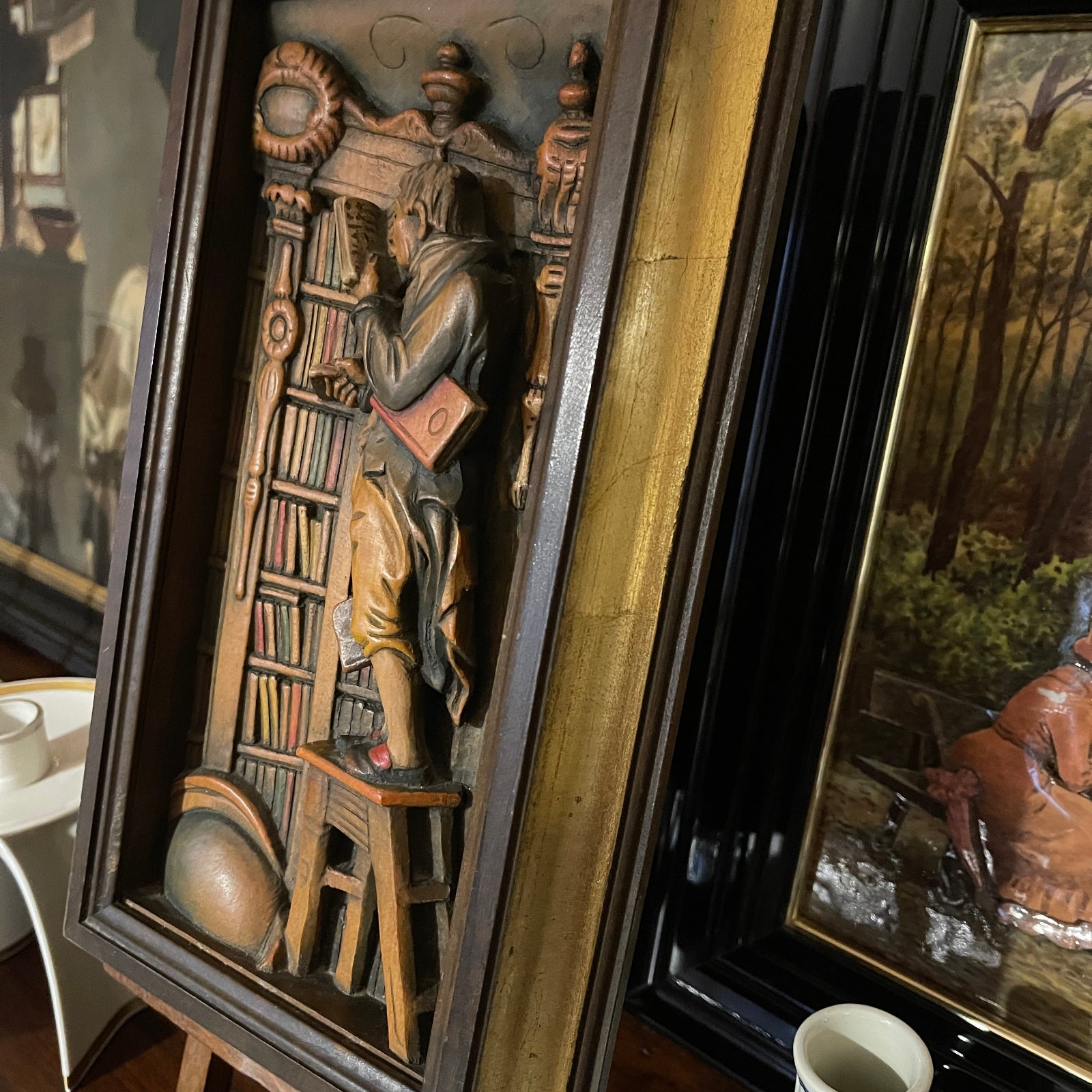 Decorative wall art with a person reading a book in a library setting, surrounded by other artworks.
