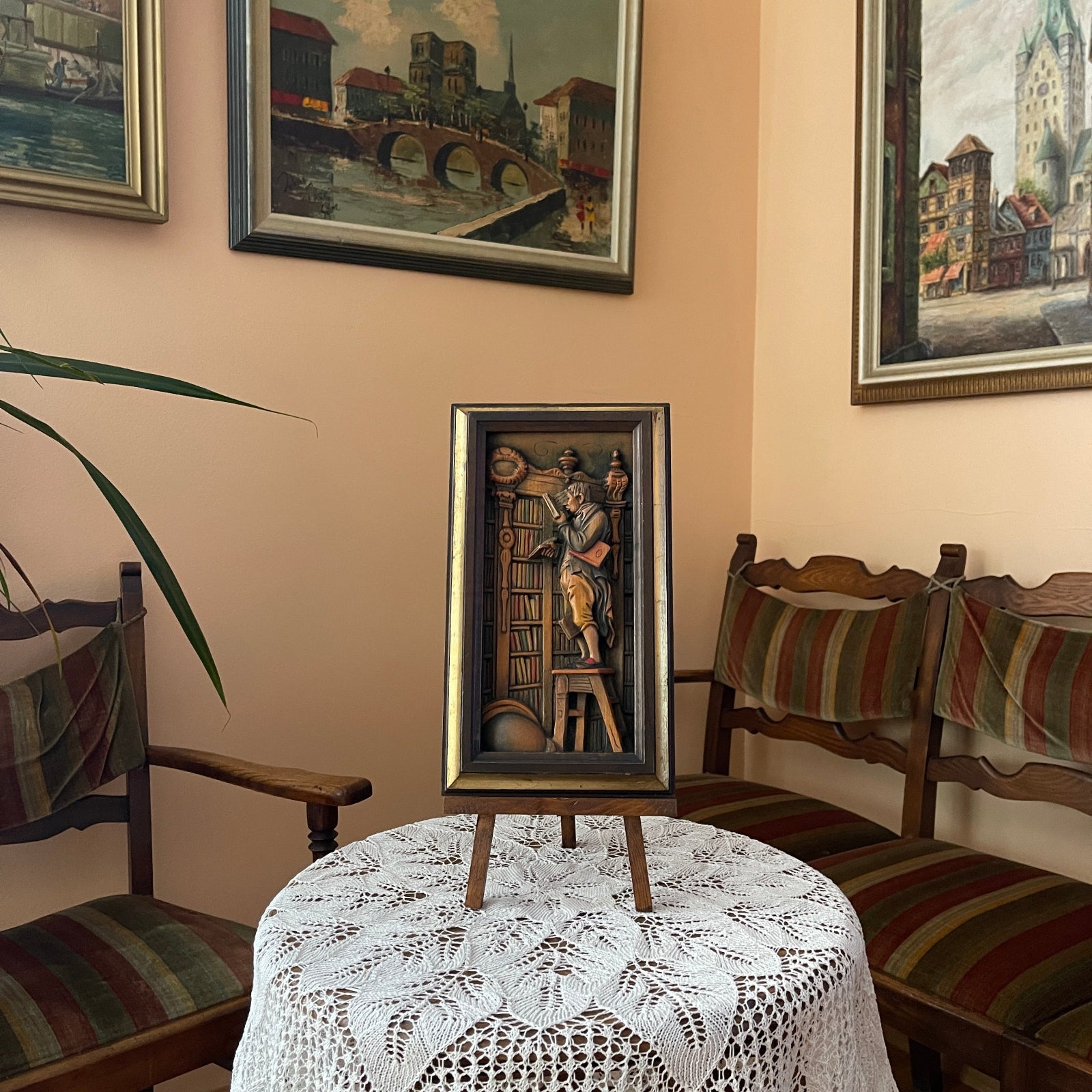 Small framed artwork on a stand in a room with striped chairs and lace tablecloth.