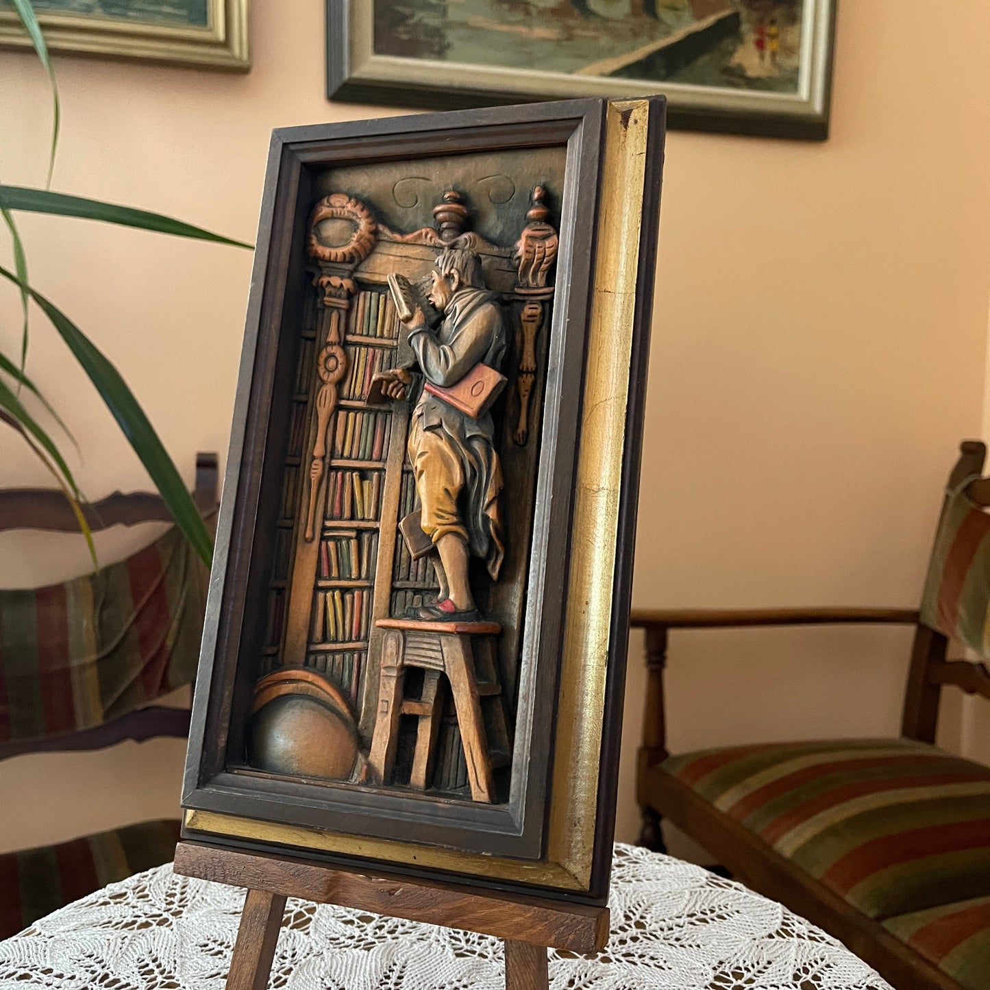 Decorative wall art of a man reading a book in a library setting on a stand.