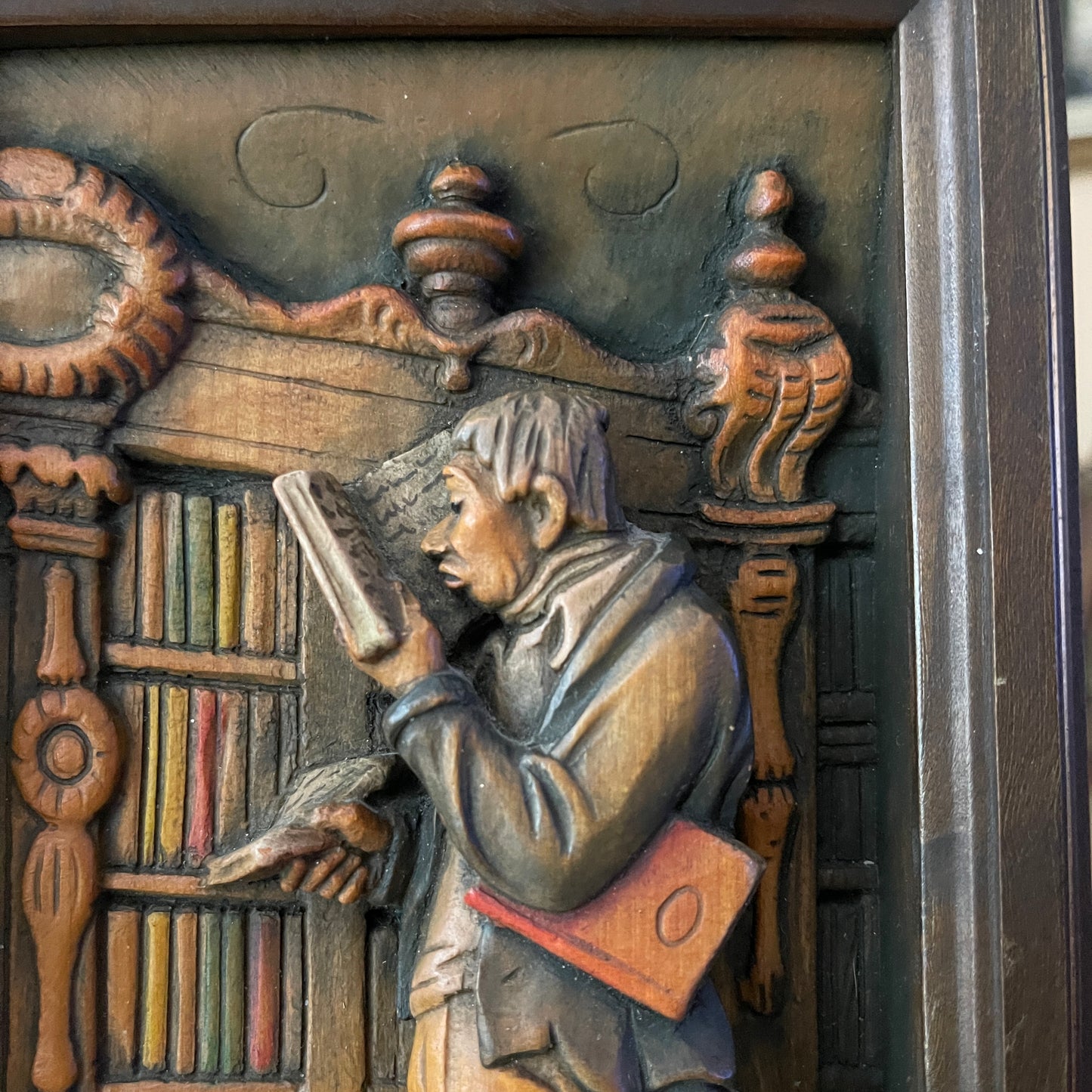Carved wooden panel depicting a person reading with books and decorative elements.