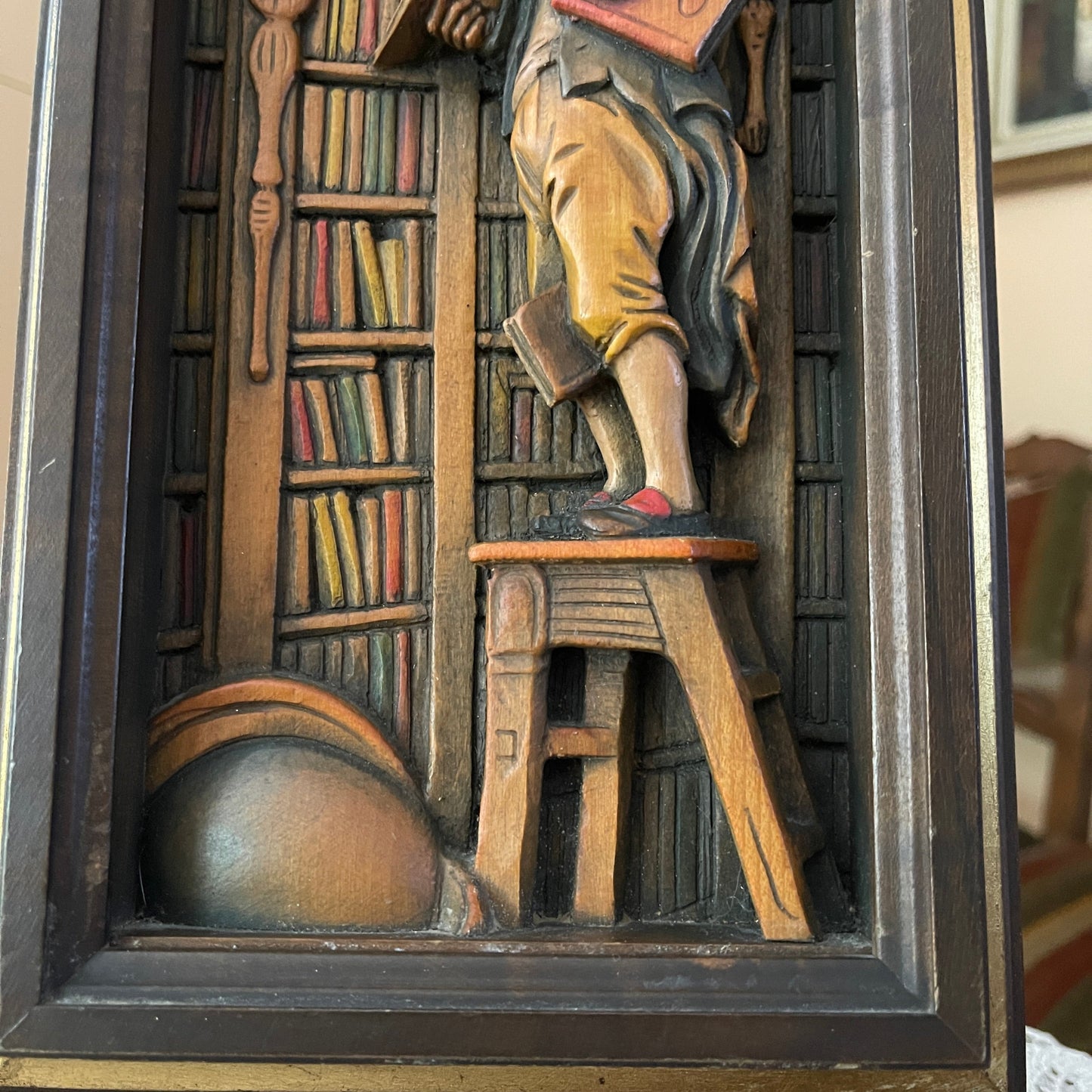 Wooden relief sculpture of a person reading a book in a library setting