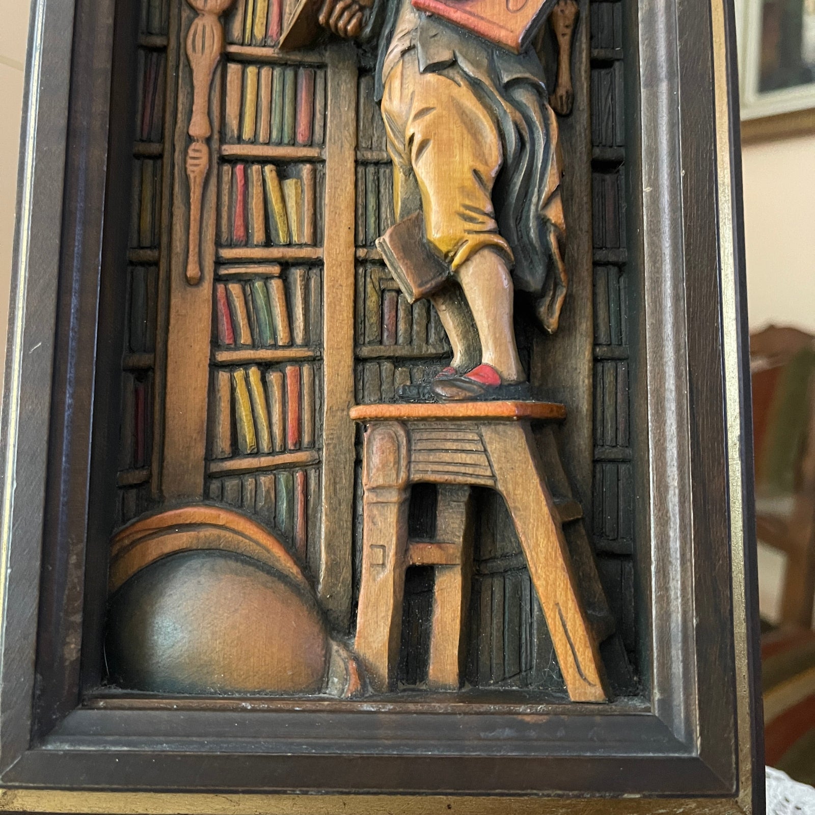 Wooden relief sculpture of a person reading a book in a library setting