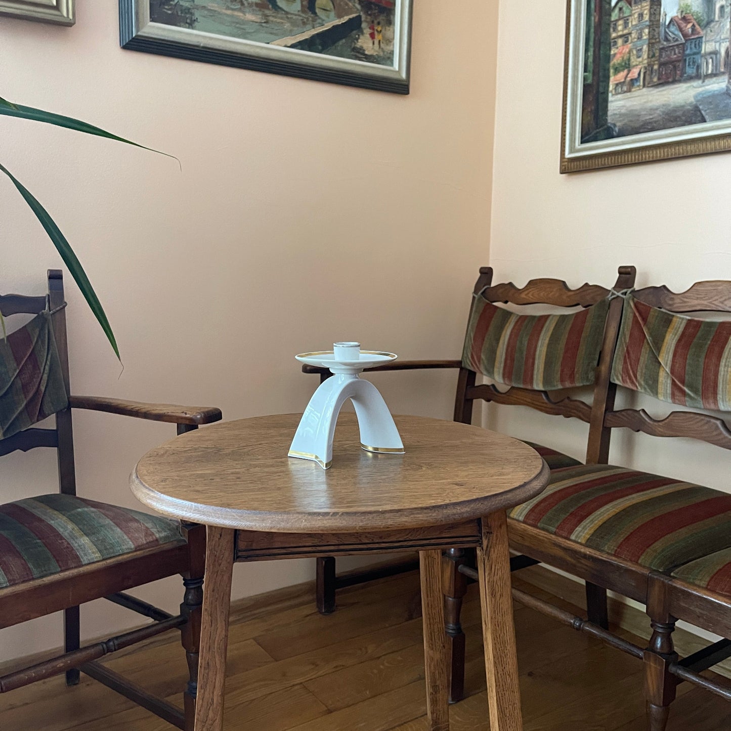 Round wooden table with a white candle holder in a room with striped cushioned chairs and framed pictures on the wall.